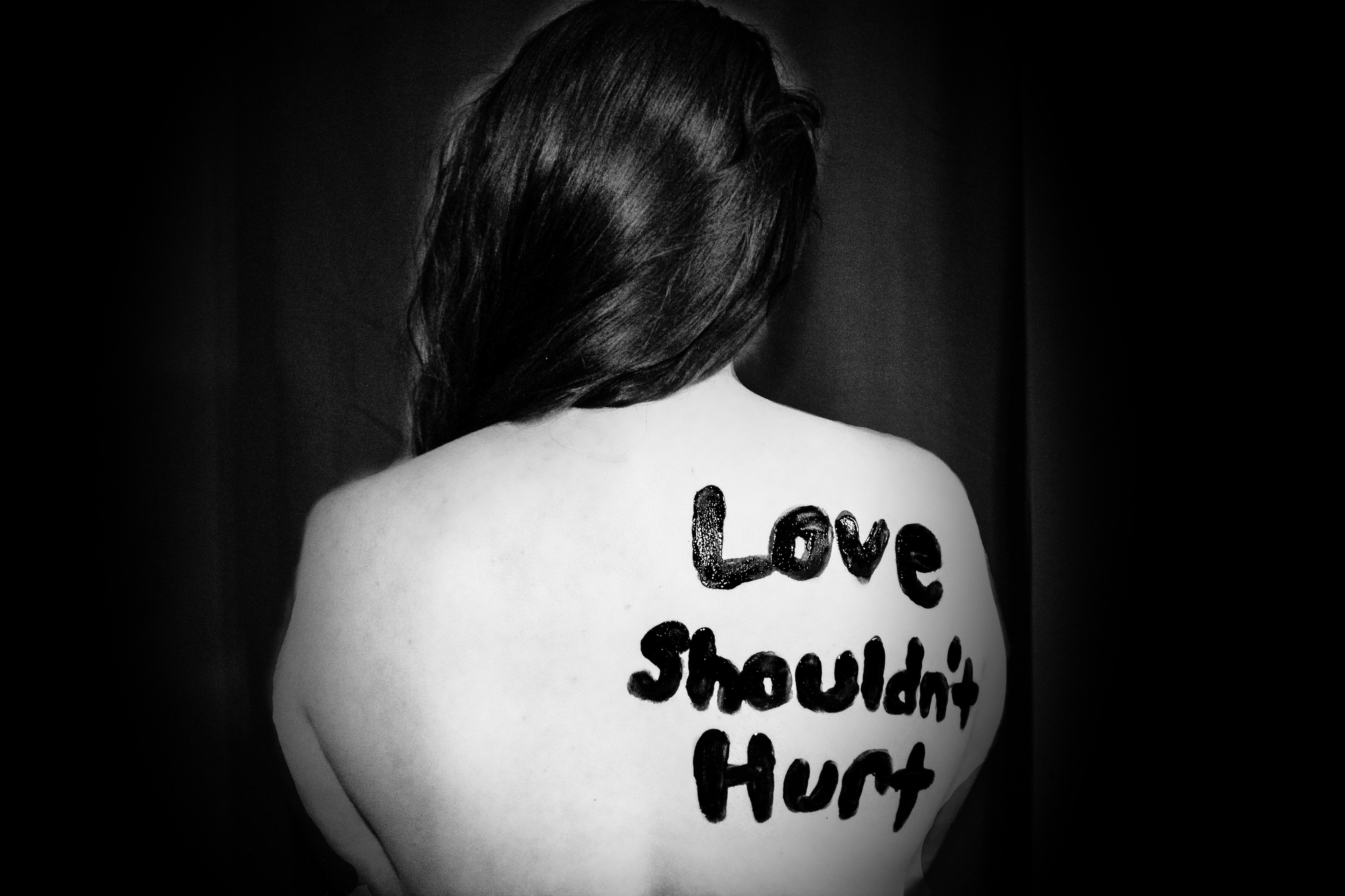 Woman with paint on her back that says "Love shouldn't hurt"